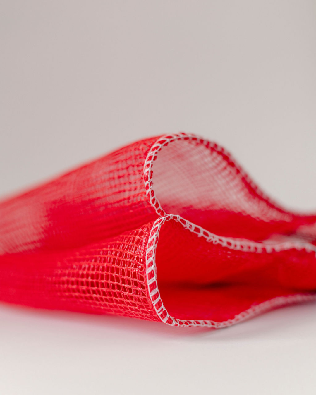 Close-up of a red mesh berley bag on a light white background