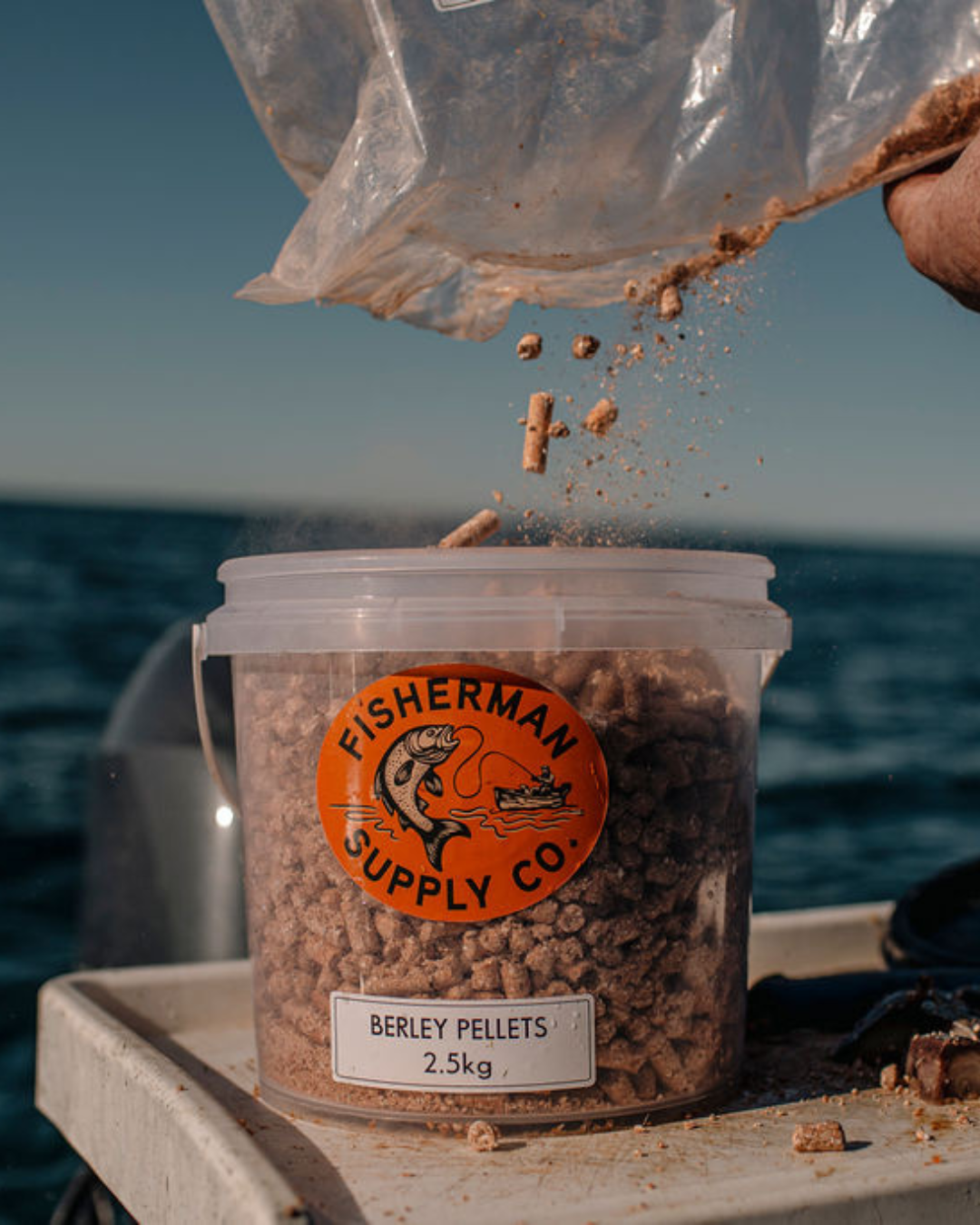 Fisherman Supply Co. berley pellets being poured from a bag into a container on a boat.
