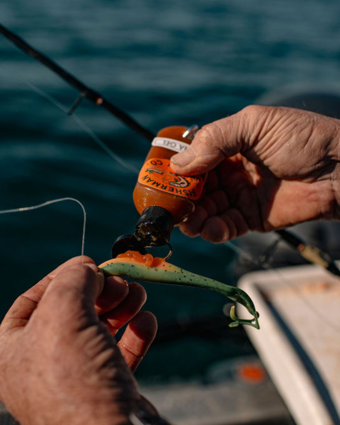 Close-up of hands tying a fishing lure to a fishing rod with water in the background