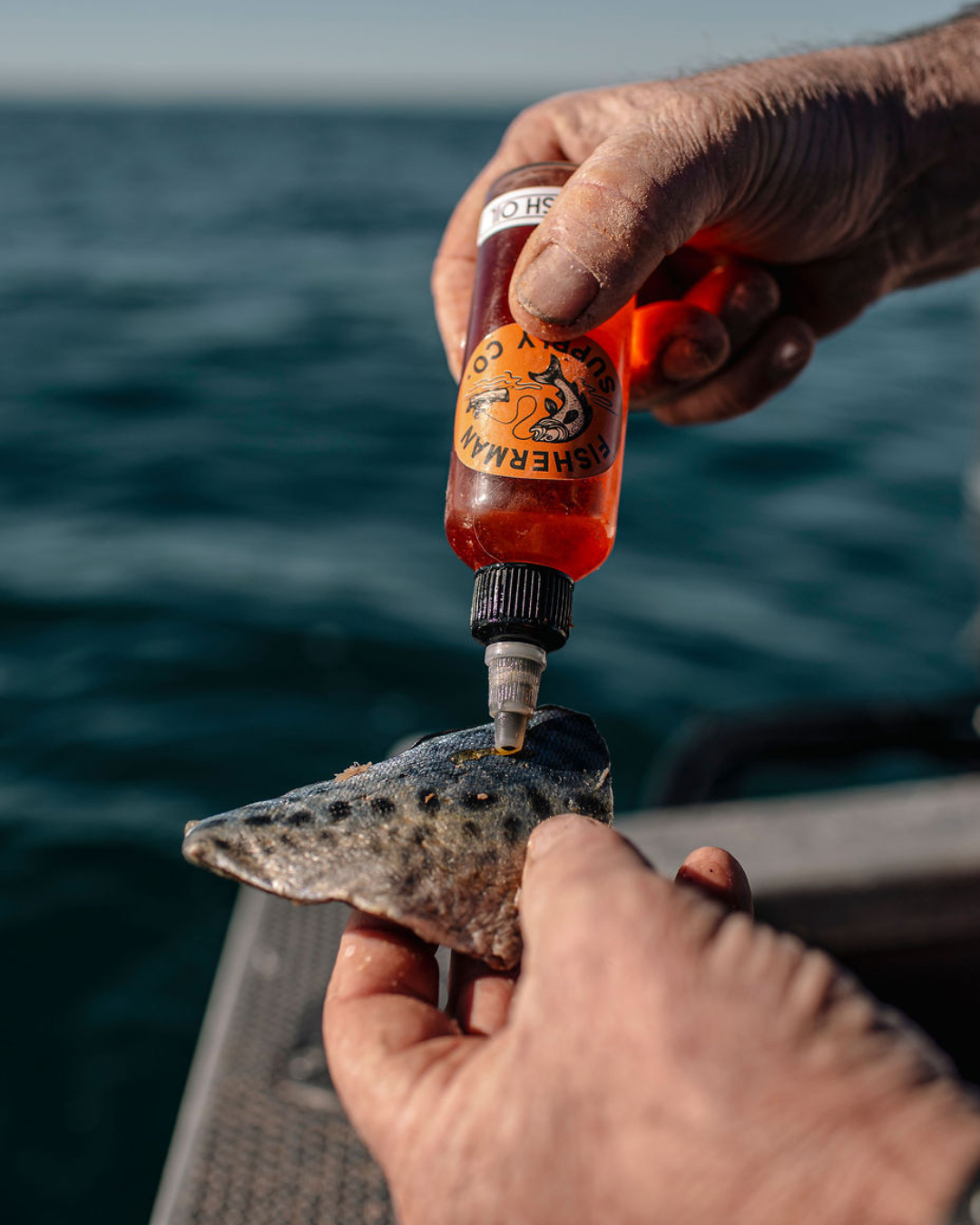 Person applying a bottle of Fish oil to fish bait on a boat with ocean in the background